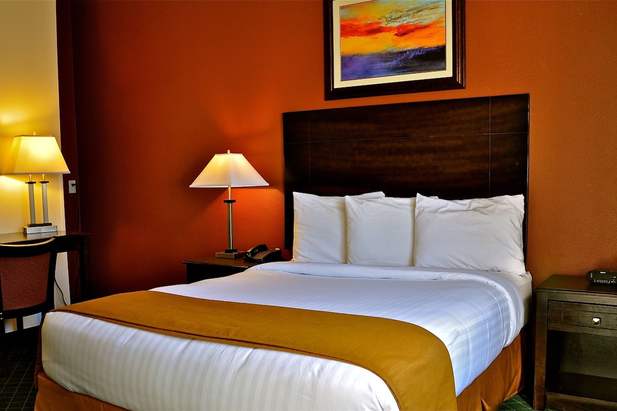 A hotel room with a large bed, two bedside tables, a desk with a lamp, and a painting on the wall.