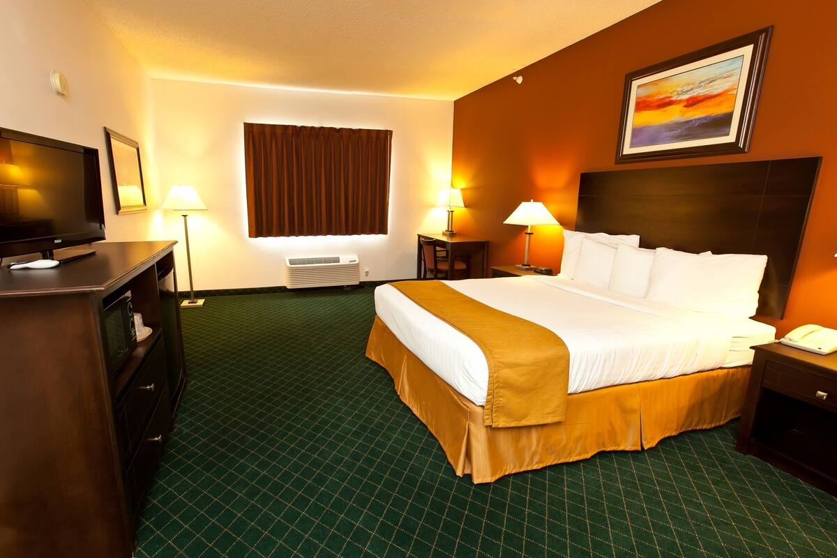 A hotel room with a large bed, two bedside lamps, a flat-screen TV, a desk with a lamp, and a painting on the wall.
