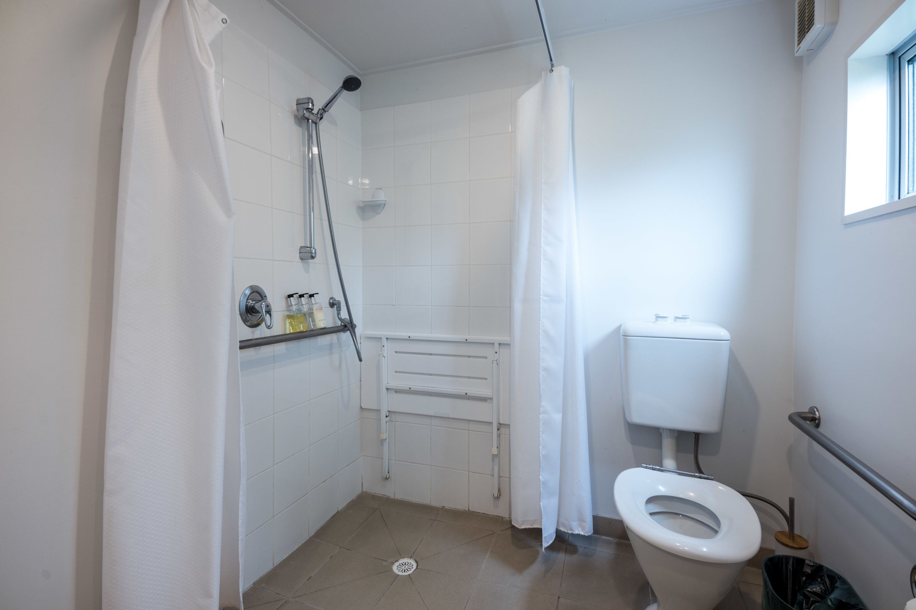 A small, white bathroom with a shower, toilet, and a window.