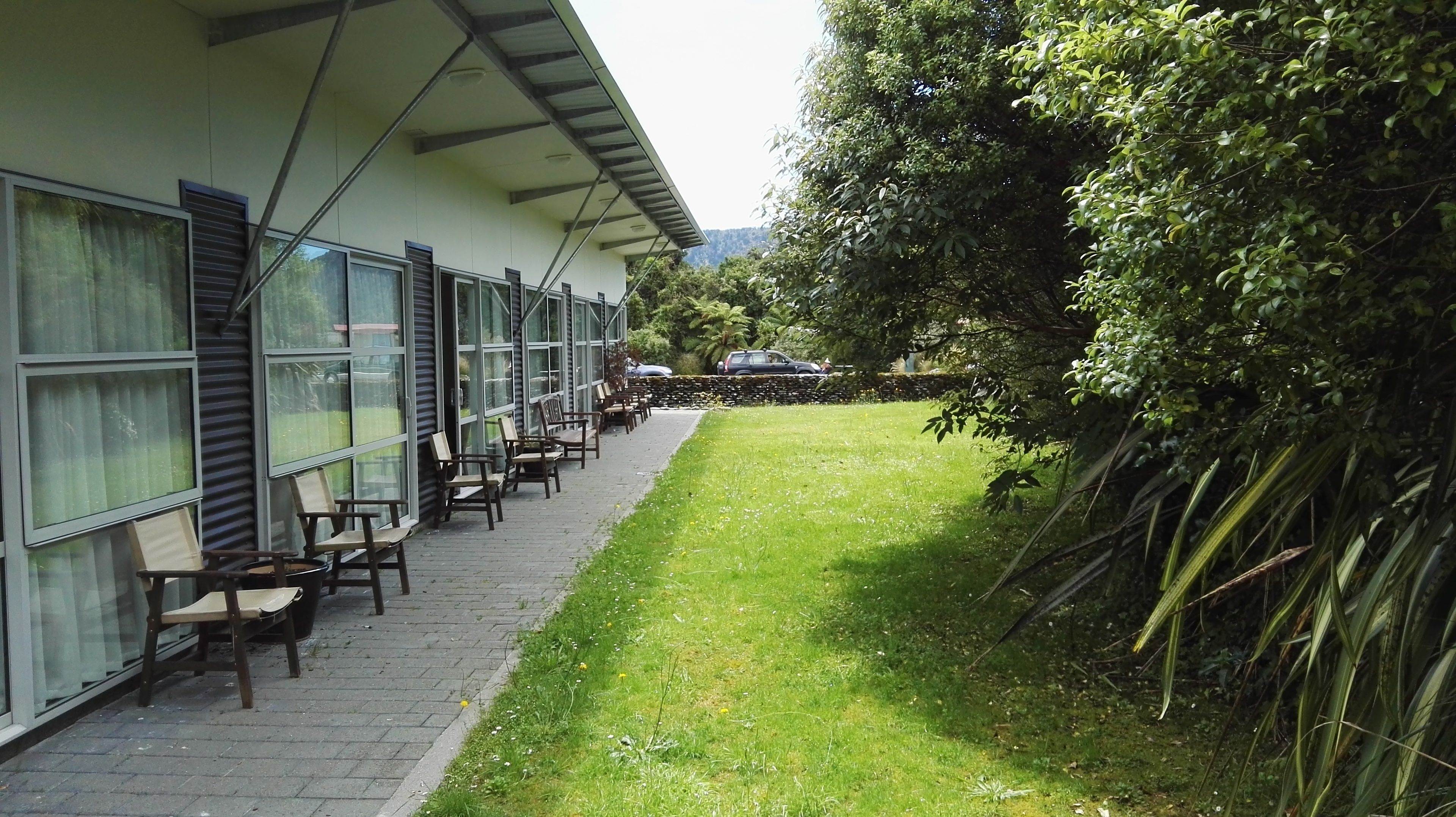 A building with a covered outdoor seating area, a paved walkway, and a grassy lawn.