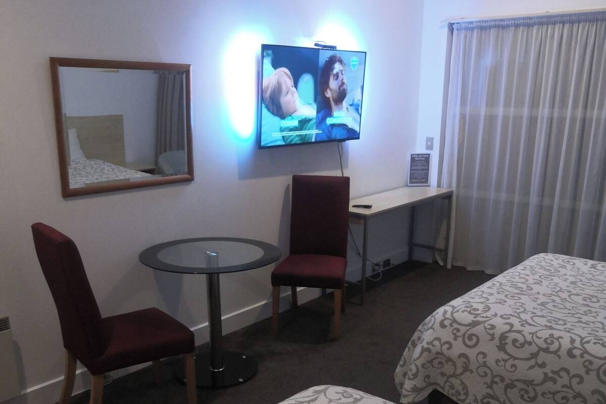 Habitación de hotel con dos camas, un escritorio, una silla, un televisor y un espejo.
