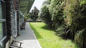 A pathway leading to a building with stone walls and a covered area with benches. - The Westhaven Motel (Fox Glacier)