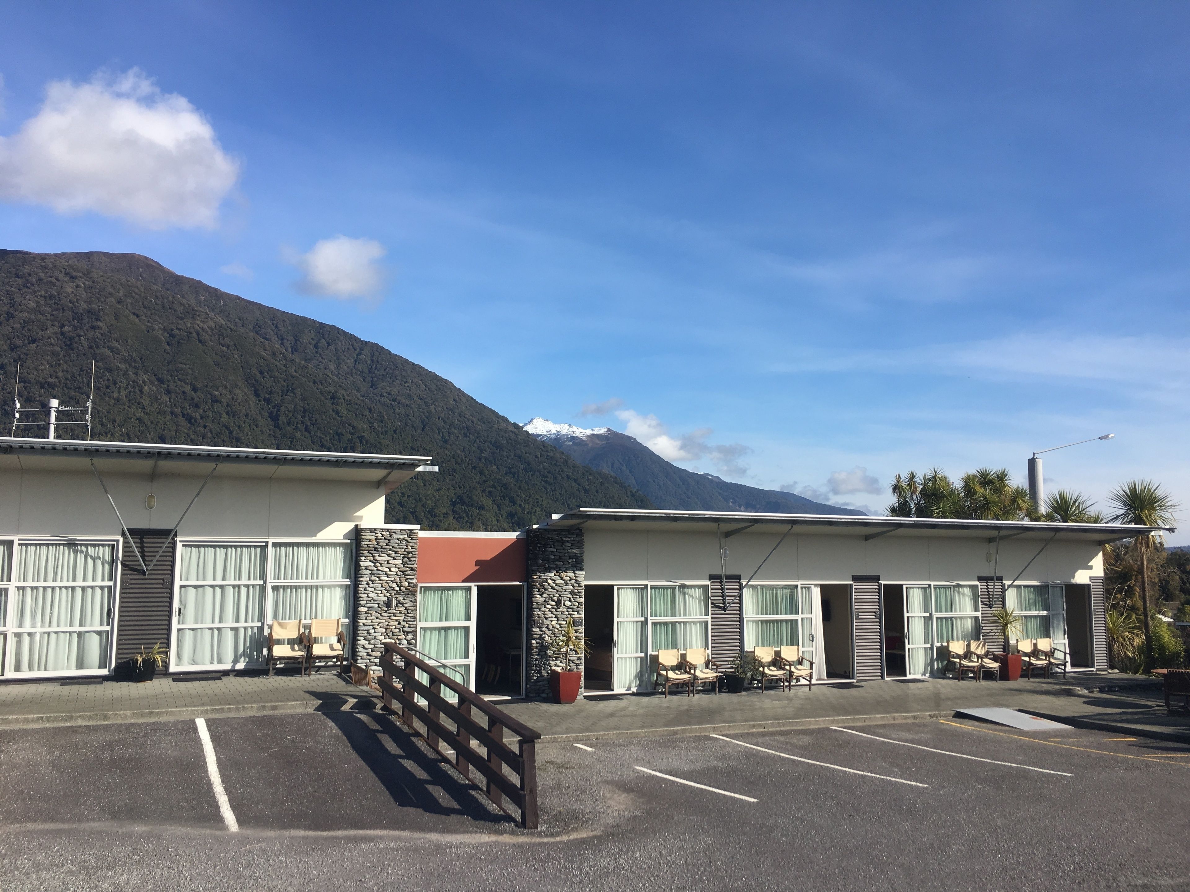 A hotel with a parking lot, outdoor seating, and a mountain backdrop.