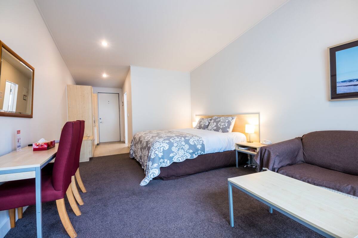 Una habitación de hotel con cama, escritorio, silla, sofá y mesita de noche.