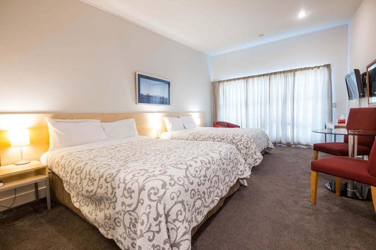 Habitación de hotel con dos camas, un escritorio con silla, televisor y ventana con cortinas.