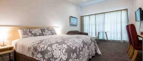 A hotel room with a large bed, a desk, a chair, and a television.