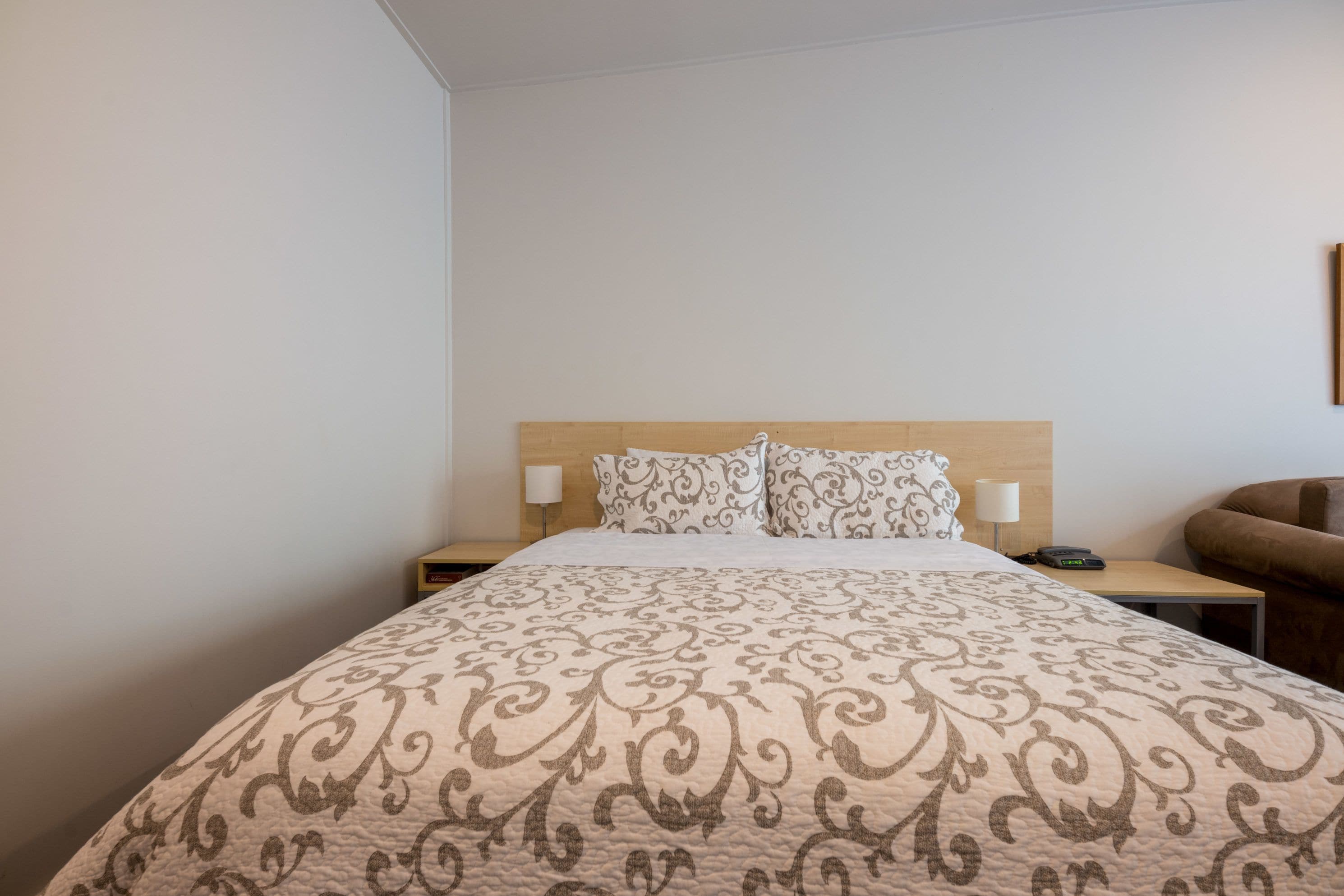 A hotel room with a large bed, two bedside tables, a lamp, and a brown armchair.