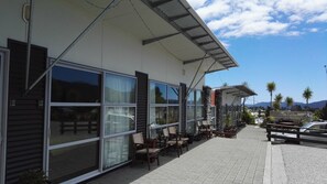 A building with large windows, outdoor seating, and a view of palm trees and mountains. - The Westhaven Motel (Fox Glacier)