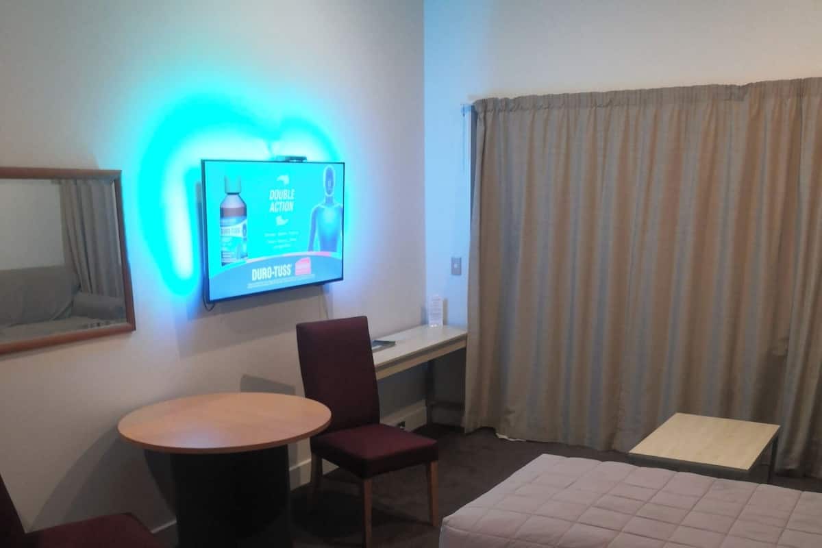 Habitación de hotel con cama, escritorio, silla, televisión y ventana con cortinas.