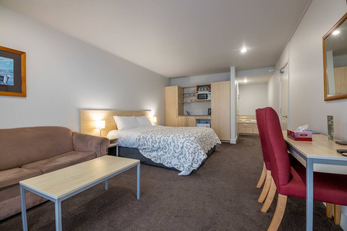 Una habitación de hotel pequeña con cama, escritorio, silla, sofá y una zona de kitchenette.