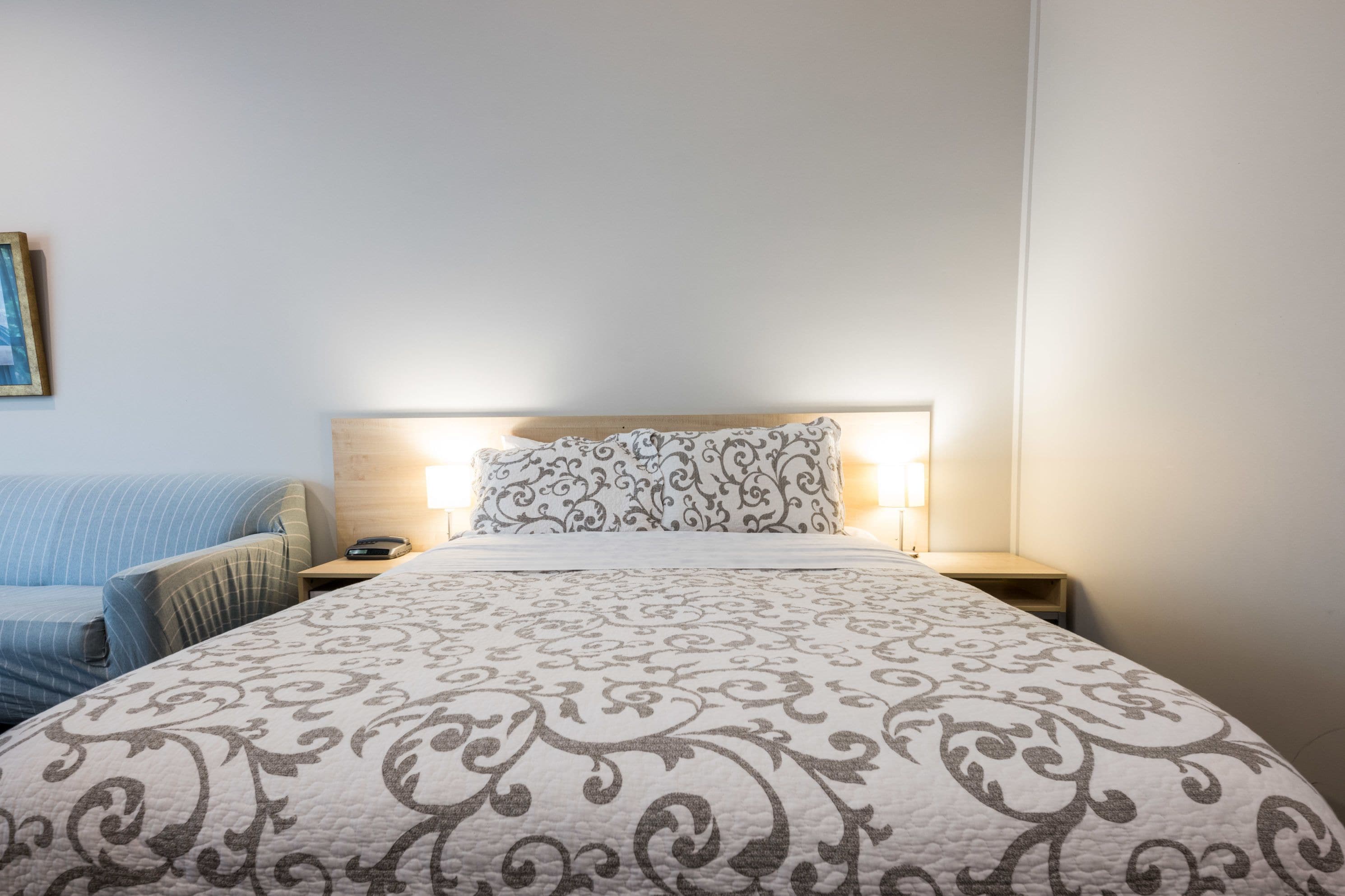 A neatly made bed with a patterned bedspread, a bedside lamp, and a blue striped chair.