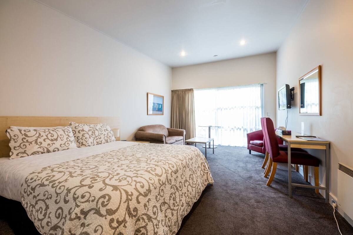 Una habitación de hotel con una cama grande, un escritorio con silla, una mesita y un televisor montado en la pared.