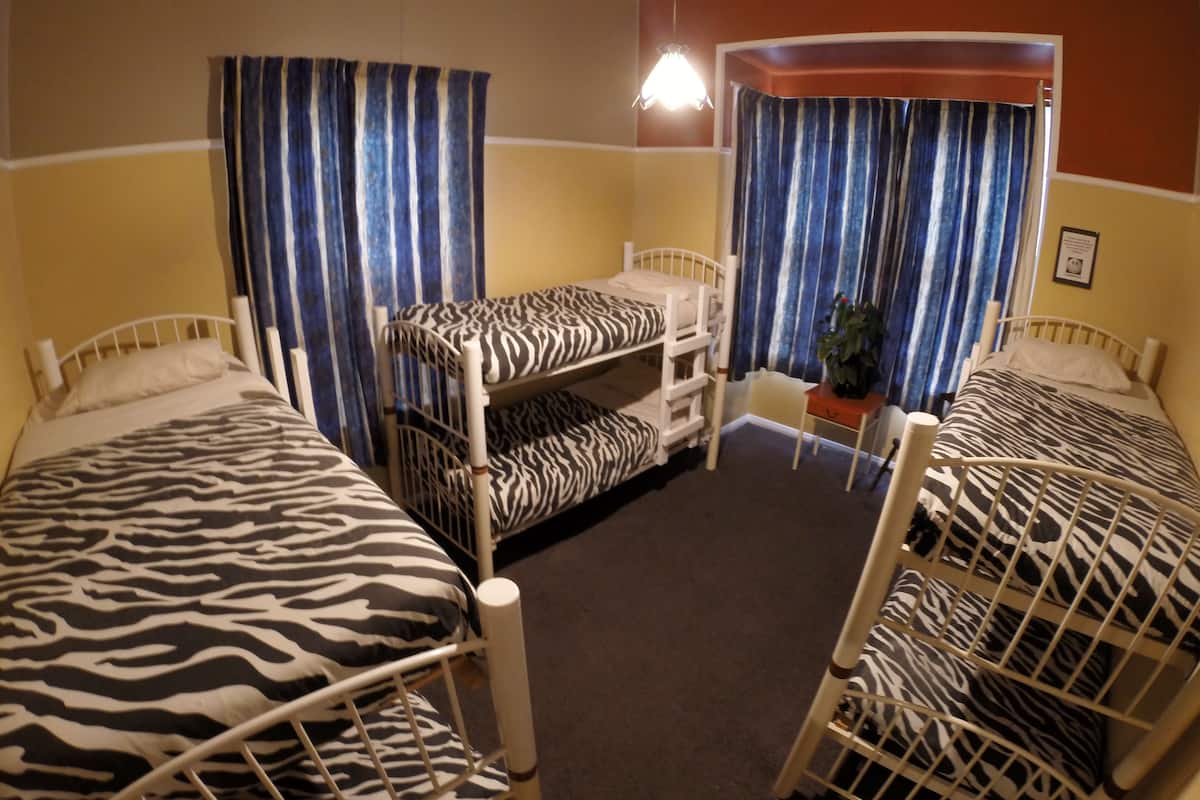 Ein Zimmer mit Etagenbetten, gestreifter Vorhängen, einem kleinen Tisch mit einer Pflanze und einem gerahmten Bild an der Wand.