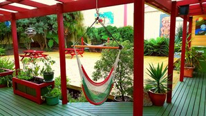 A covered patio area with red wooden beams, a hammock, and potted plants. - Bazil's Hostel & Surf School (Westport)