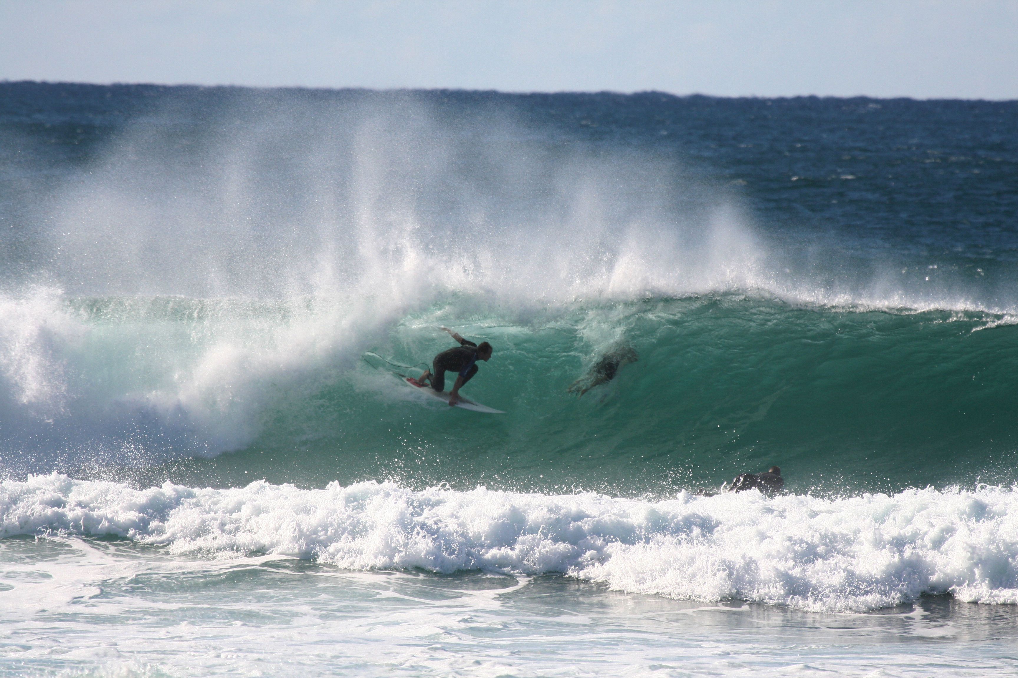 Un surfista cabalgando una ola grande, con otros surfistas al fondo.