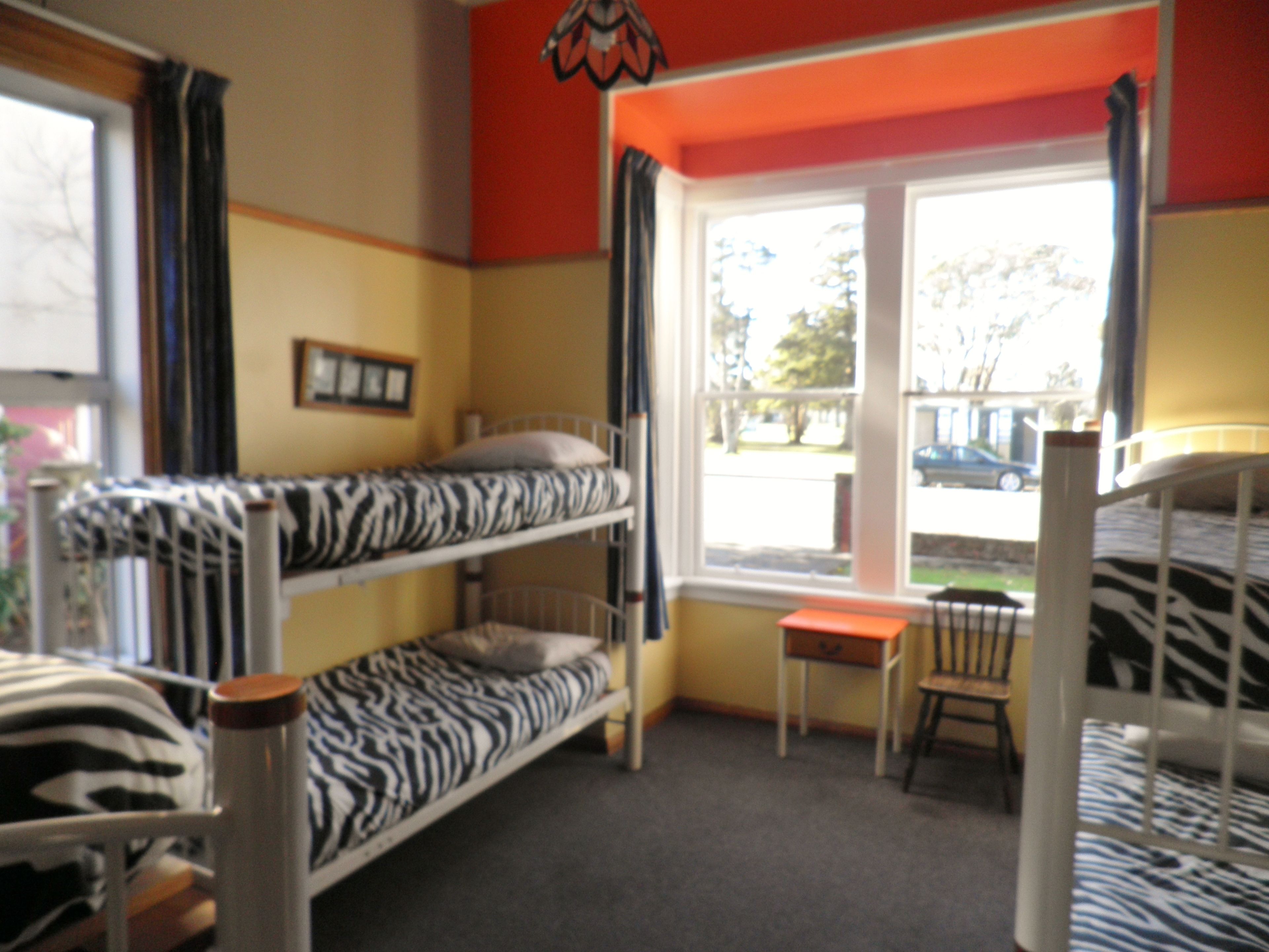 A room with bunk beds, a window with curtains, a small table, and a chair.