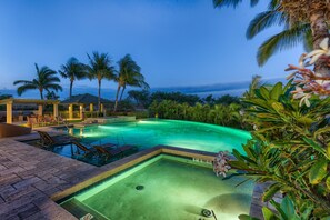 Una piscina con sillas de descanso y una zona de estar cubierta, rodeada de palmeras y exuberante vegetación.
