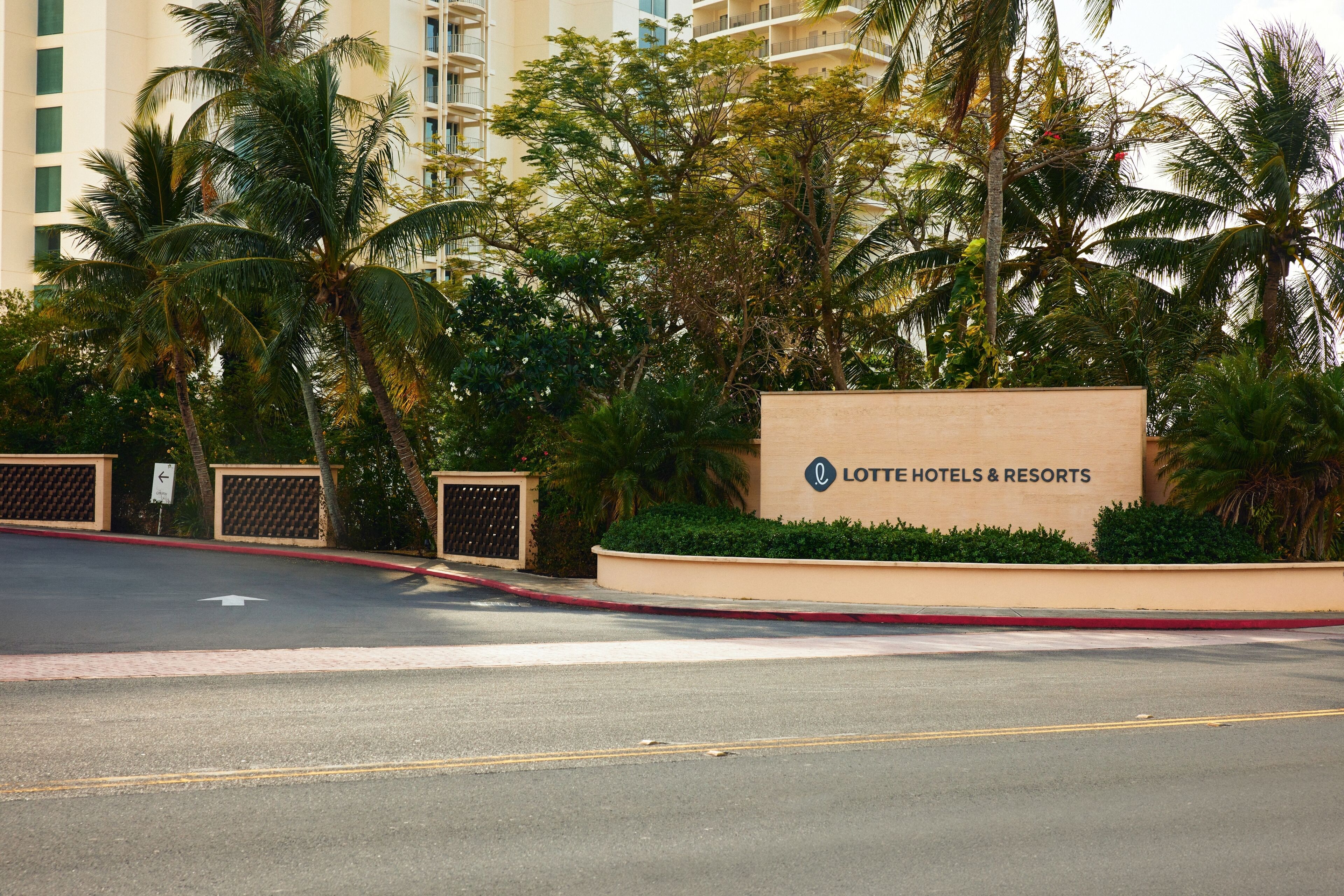 A sign for Lotte Hotels & Resorts with a clear view of the surrounding palm trees and a road in the foreground.