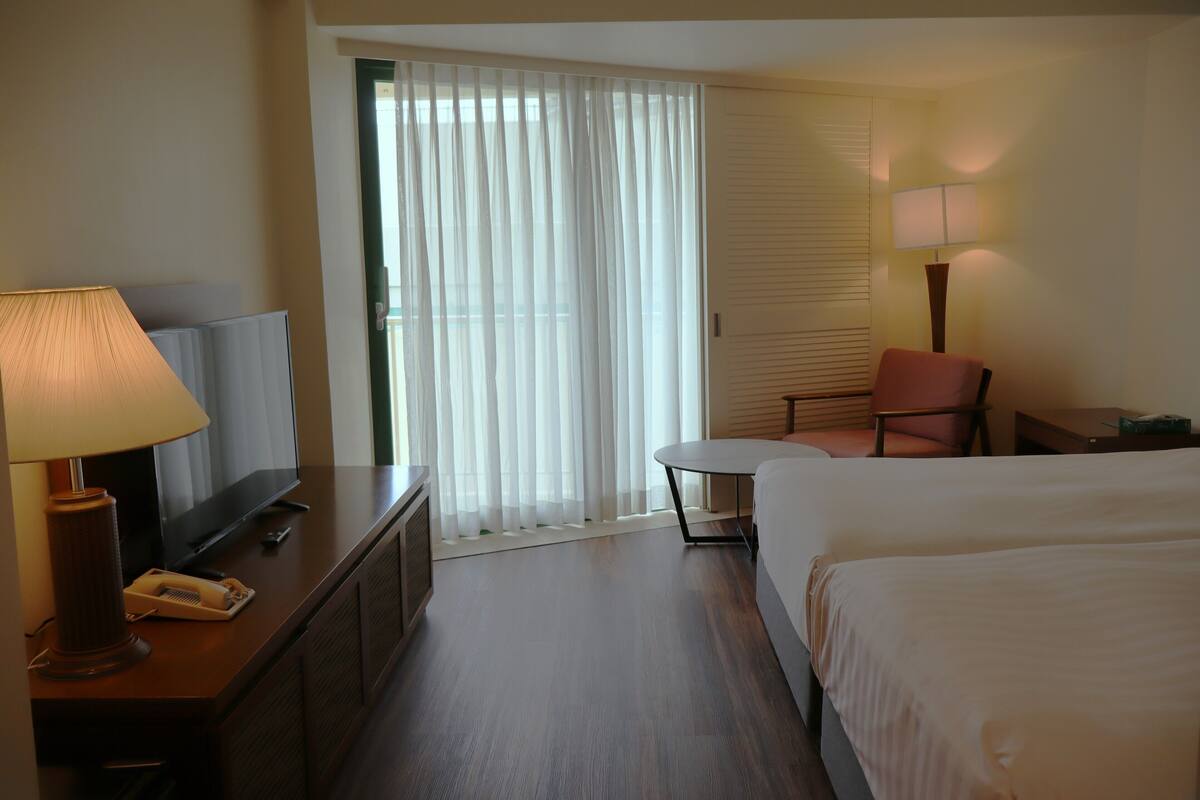A hotel room with a bed, a desk with a lamp, a chair, a TV, and a window with curtains.