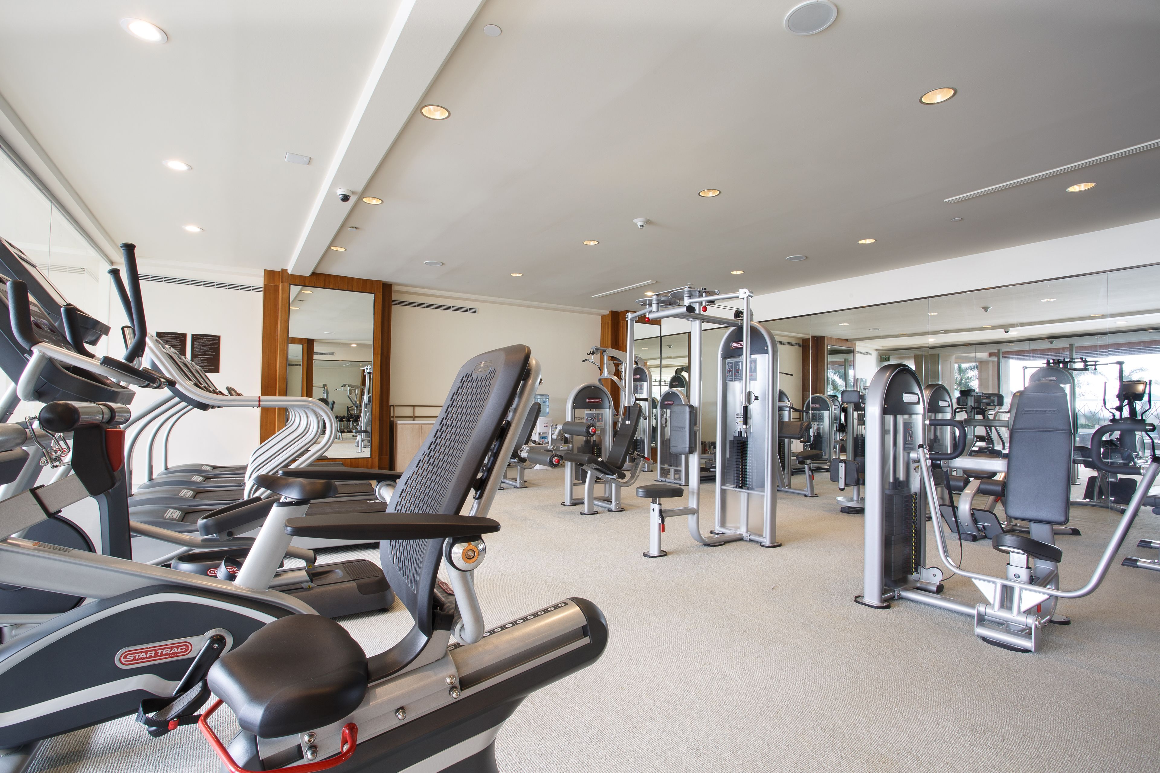 Un gimnasio con cintas de correr, máquinas de pesas y un espejo.
