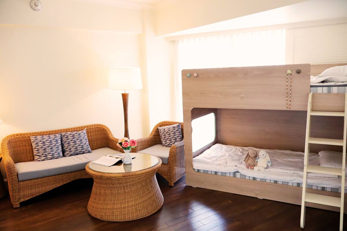 A room with a bunk bed, a sofa, a round wicker table, and a lamp.