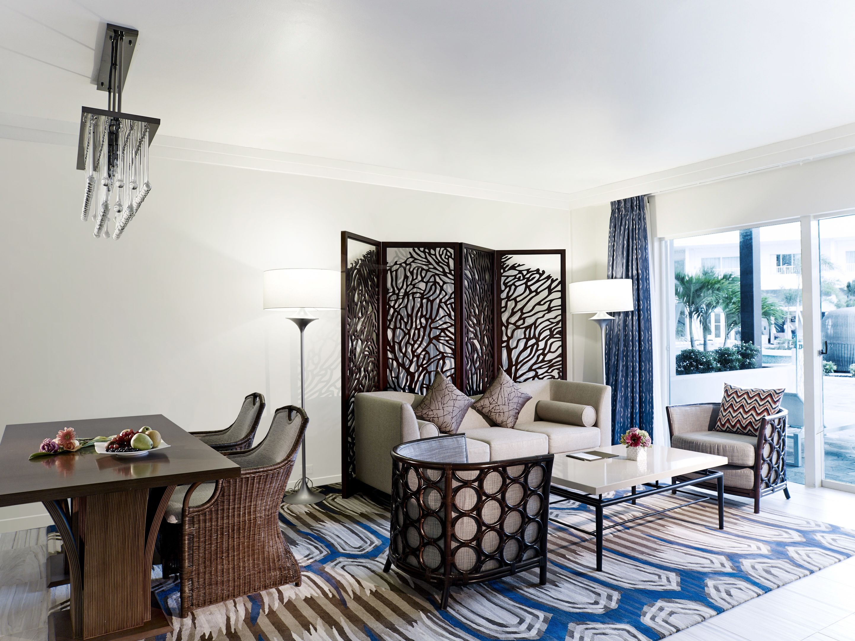 A modern hotel room with a dining area, a sofa set, a coffee table, and a decorative partition.