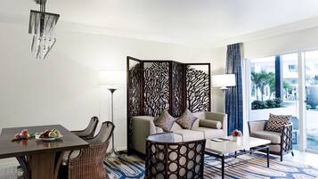 A modern hotel room with a dining area, a sofa set, a coffee table, and a decorative partition.
