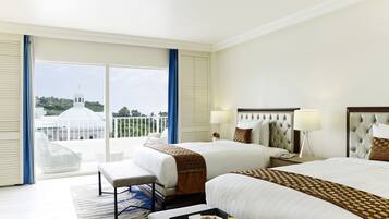 Habitación de hotel con dos camas, un ventanal con vistas a un edificio blanco, y una bandeja con galletas y jugo sobre la cama.