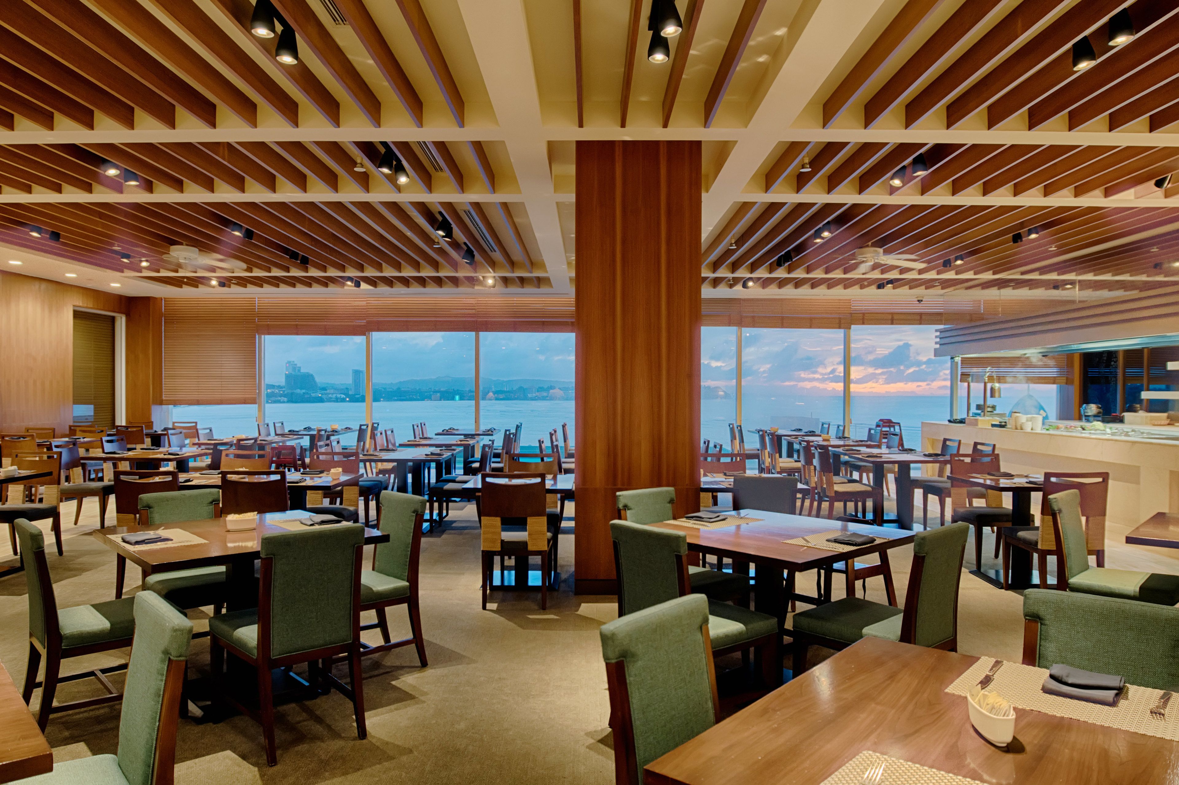 A spacious dining area with multiple tables and chairs, large windows offering a view of the sea, and a modern ceiling design.