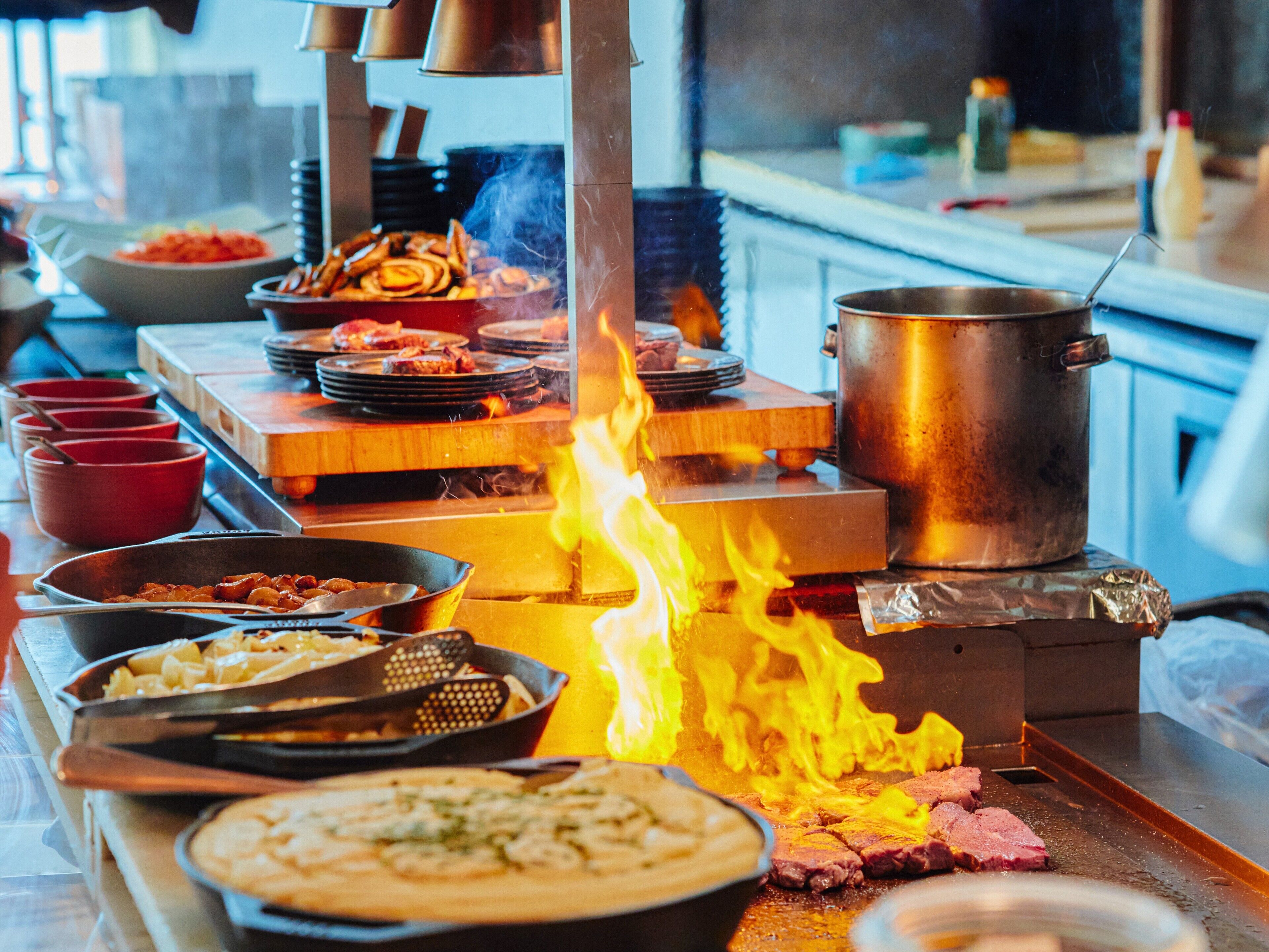 A kitchen with a large fire, cooking utensils, and various dishes.