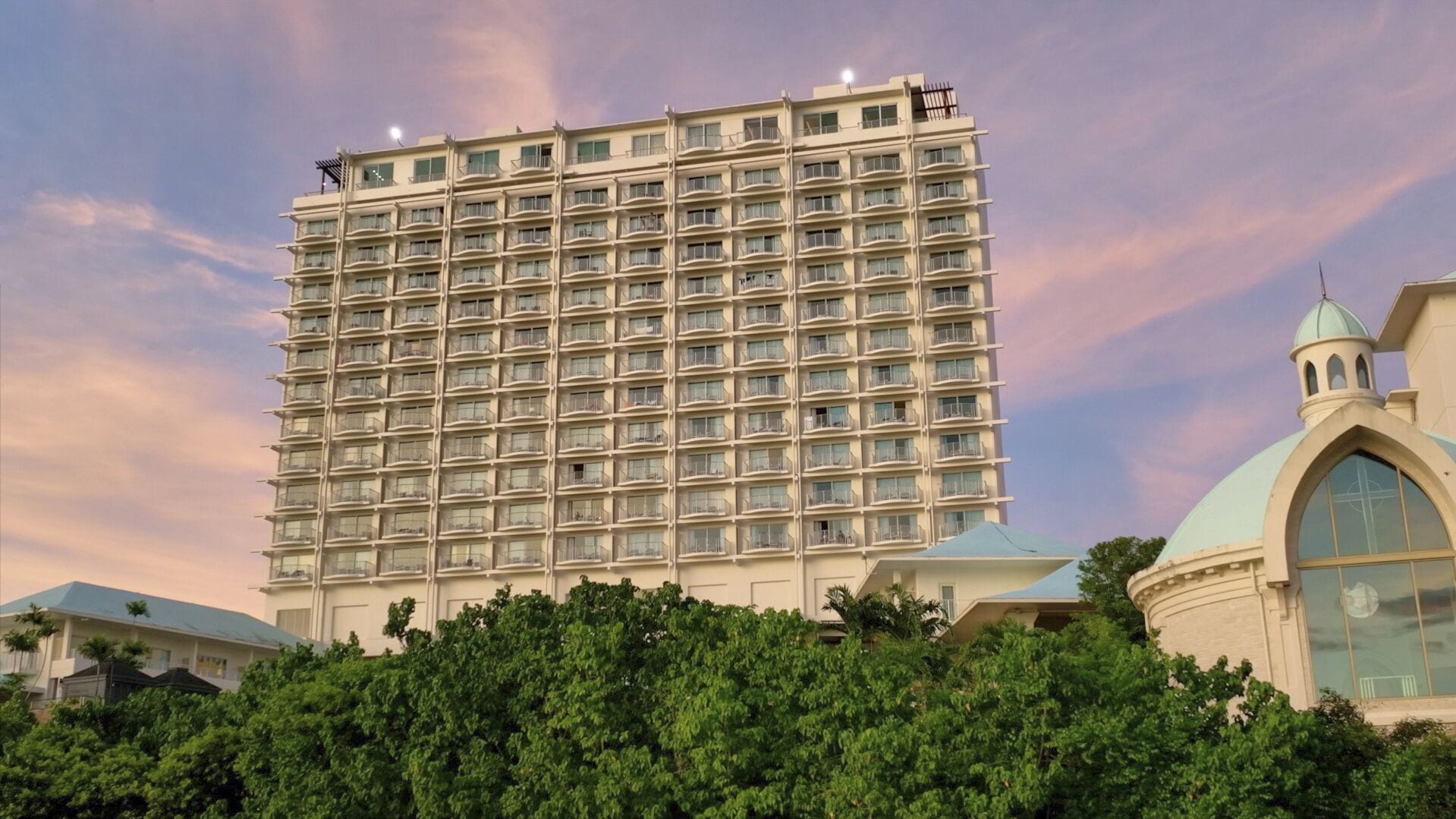 A multi-story hotel with a uniform facade, numerous balconies, and a dome structure to the right.