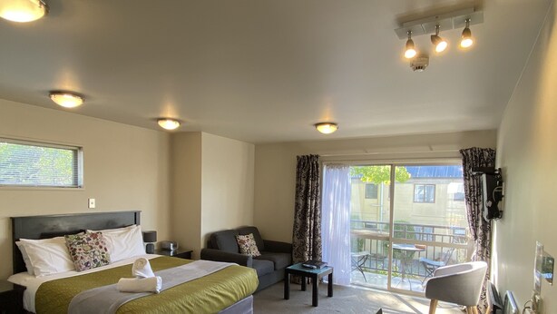 Hotelkamer met een bed, een bank, een kleine tafel en een stoel. Er is een balkon met een tafel en stoelen.