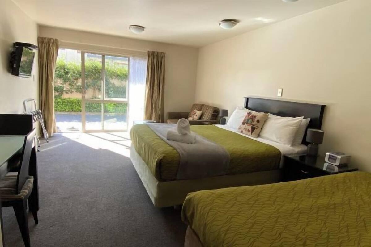 Une chambre d’hôtel avec un lit, un bureau, une chaise, une télévision et une fenêtre avec des rideaux.