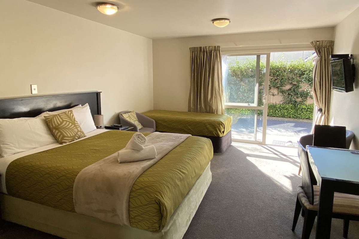 Une chambre d’hôtel avec deux lits, un bureau, une chaise et une grande fenêtre avec des rideaux.