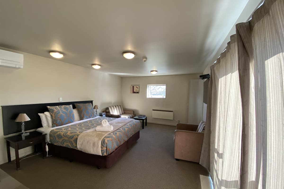 Une chambre d’hôtel avec un grand lit, un bureau, une chaise, une fenêtre et un radiateur.