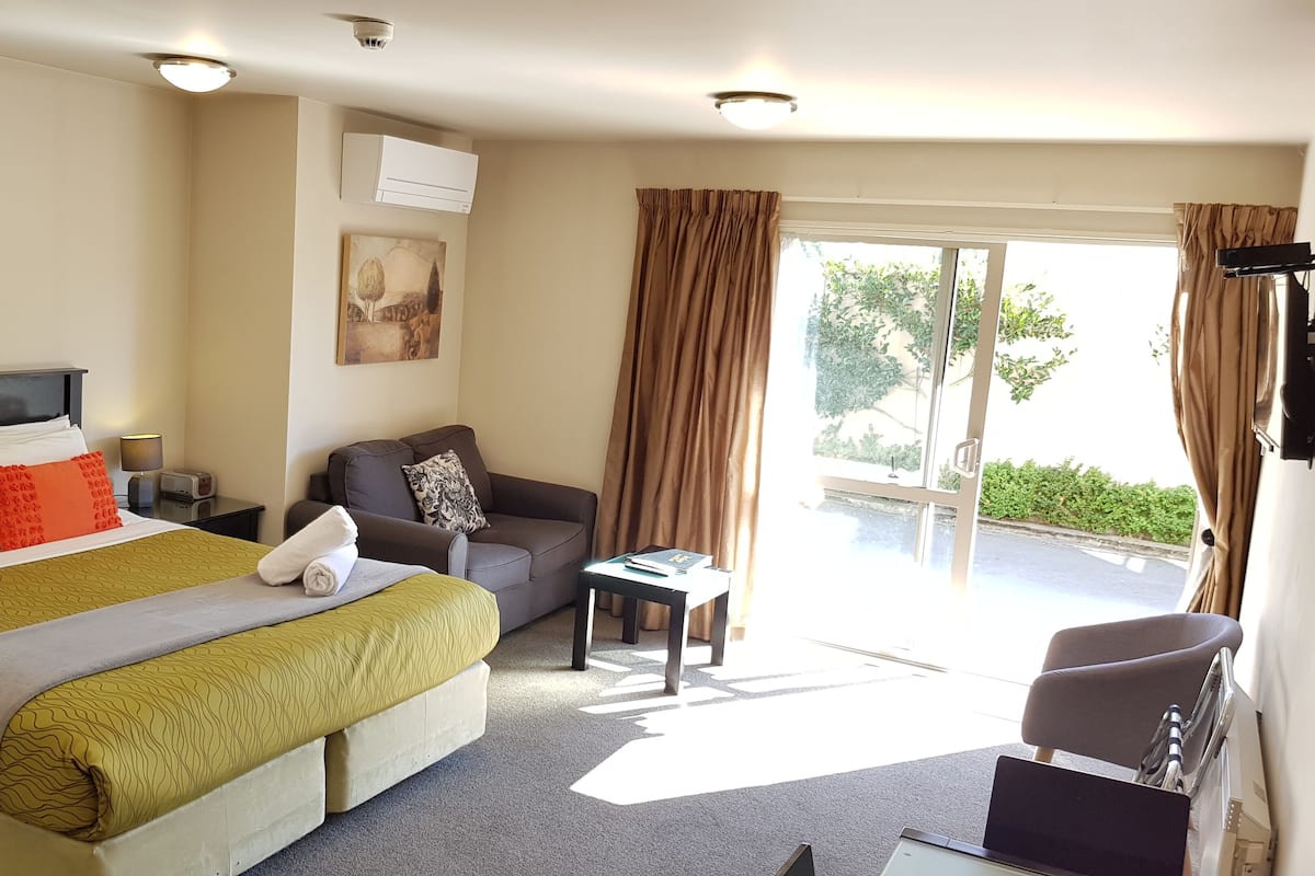 Une chambre d’hôtel avec un lit, un canapé, une petite table et une fenêtre avec des rideaux.