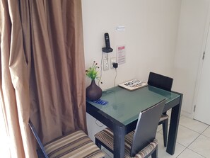 A dining area with a glass table, striped chairs, a vase with flowers, a fire safety sign, and a telephone. - De Lago Motel Apartments (Christchurch)