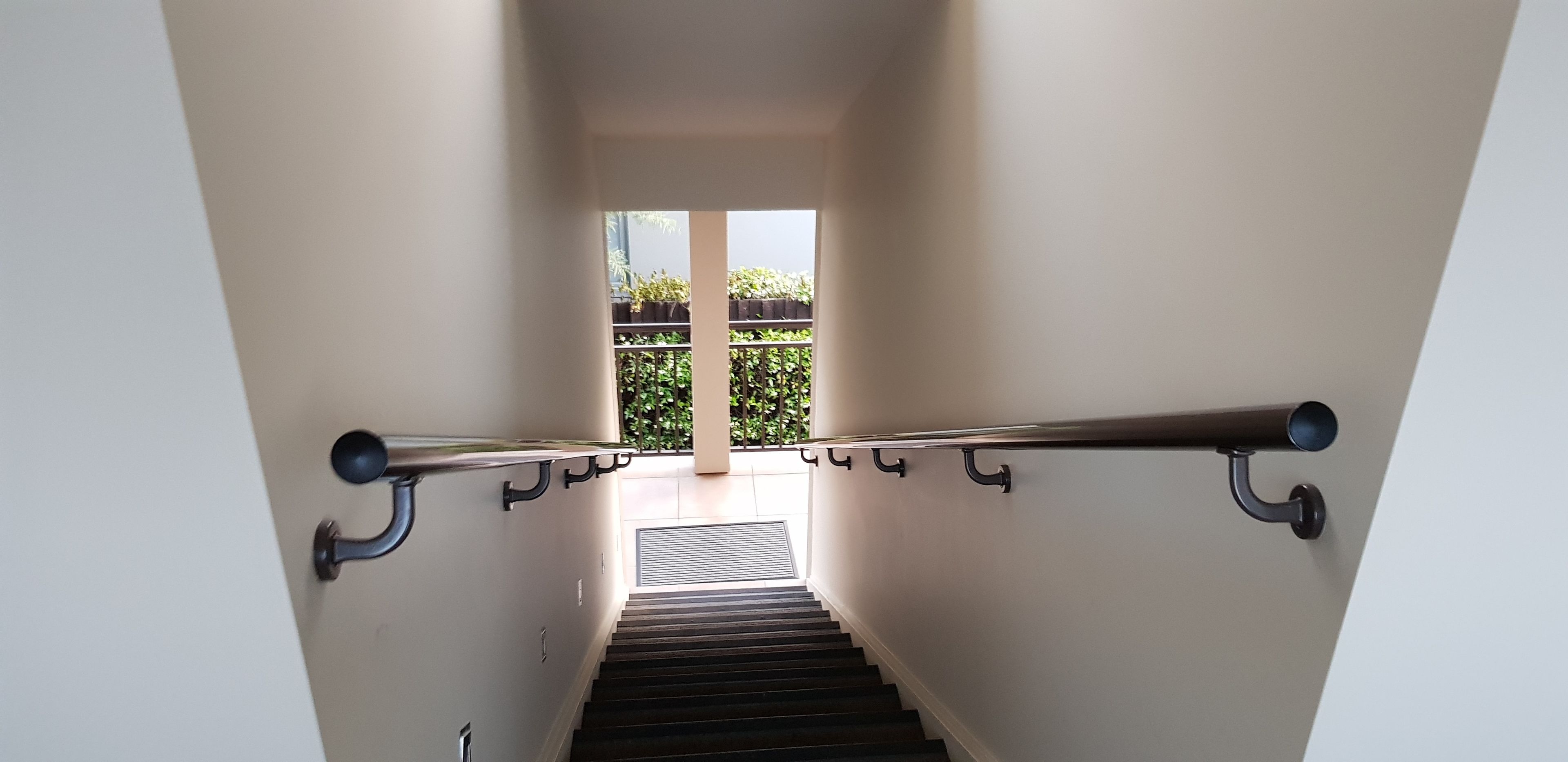 Un escalier avec des rampes en métal et une vue sur un balcon agrémenté de plantes.