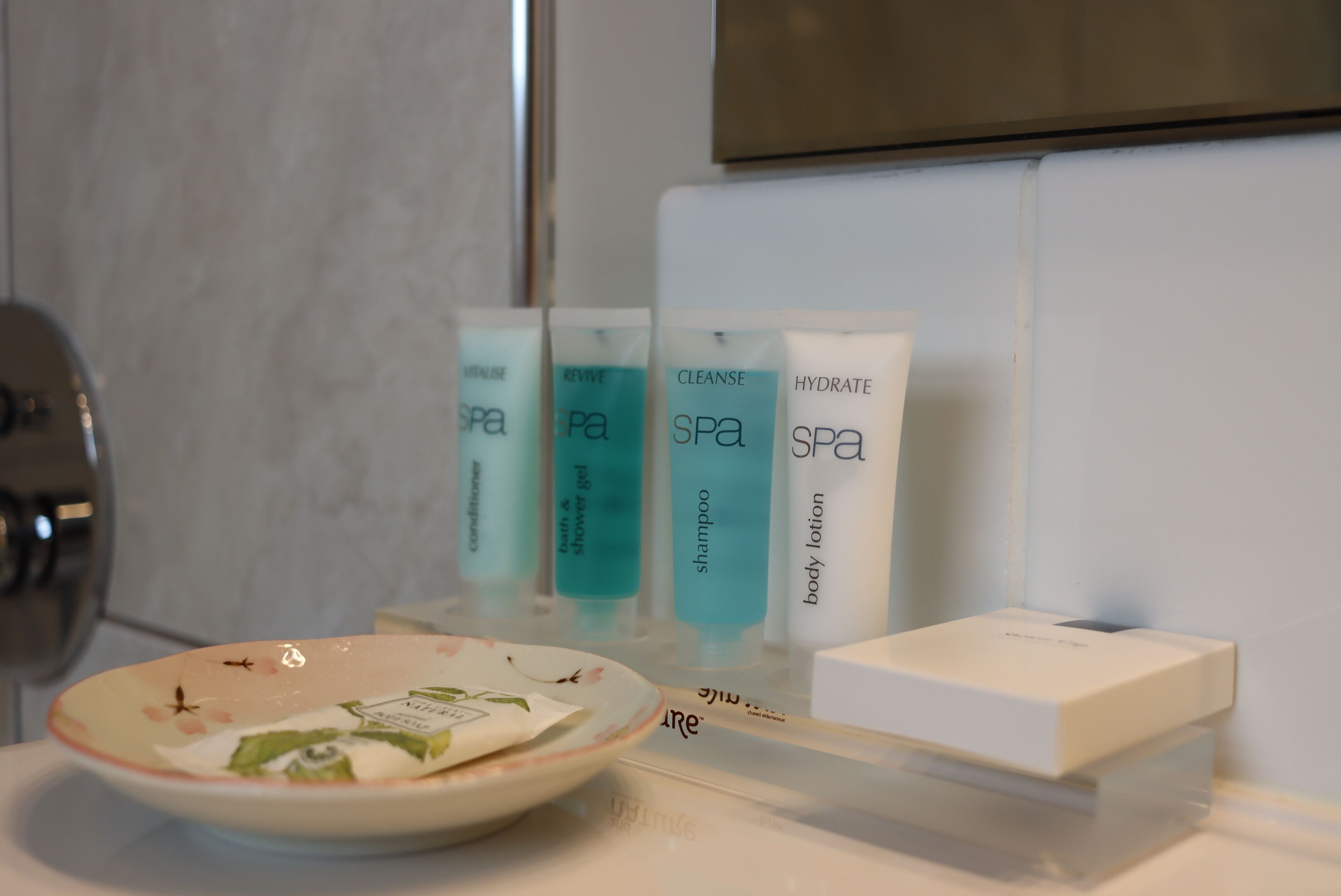 A bathroom with a sink, a mirror, and toiletries including a bowl of soap and various spa products.