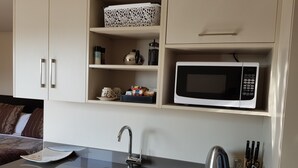 Een kleine keuken met een magnetron, spoelbak en opbergkastjes.