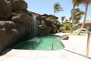 Una piscina con cascada, rodeada de rocas grandes y palmeras.