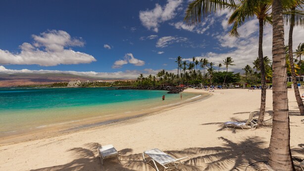 A beach with clear turquoise water, palm trees, and lounge chairs. - Fairways at Mauna Lani (Kamuela)