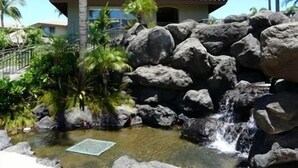 A tropical resort with a waterfall, large rocks, and palm trees. - Fairways at Mauna Lani (Kamuela)