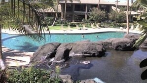 A resort with a swimming pool, palm trees, and a building with a thatched roof. - Fairways at Mauna Lani (Kamuela)