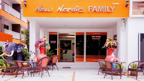 The exterior of New Nordic Family hotel with a welcoming entrance, outdoor seating area, and decorative elements like a large elephant statue and flower vases.