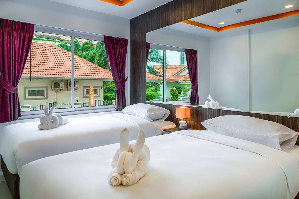 A hotel room with two beds, large windows, and a view of a red-roofed building.