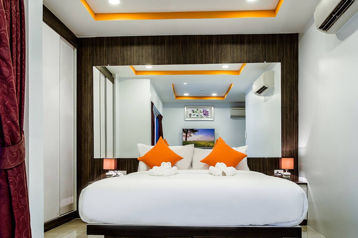 A modern hotel room with a large bed, two bedside tables, a mirror, and a ceiling with recessed lighting.