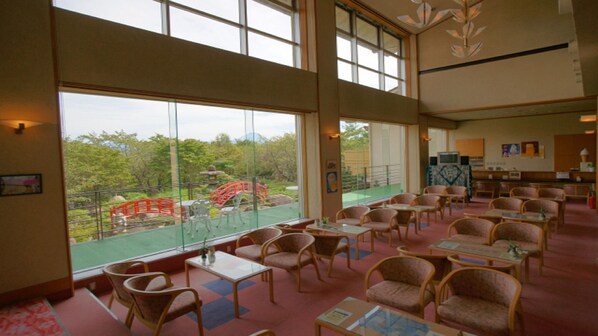 A spacious indoor area with large windows, wicker chairs, and tables.