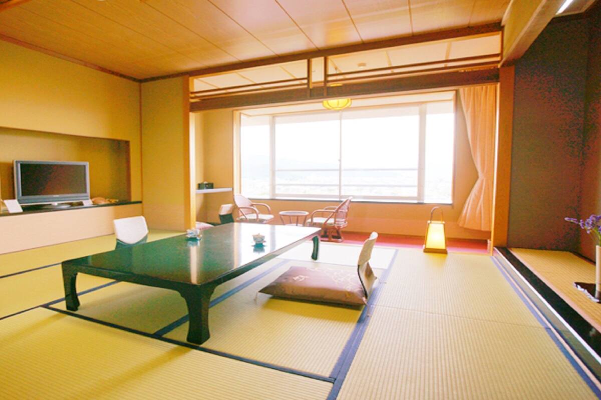 A tatami mat room with a low table, chairs, a television, and a large window.