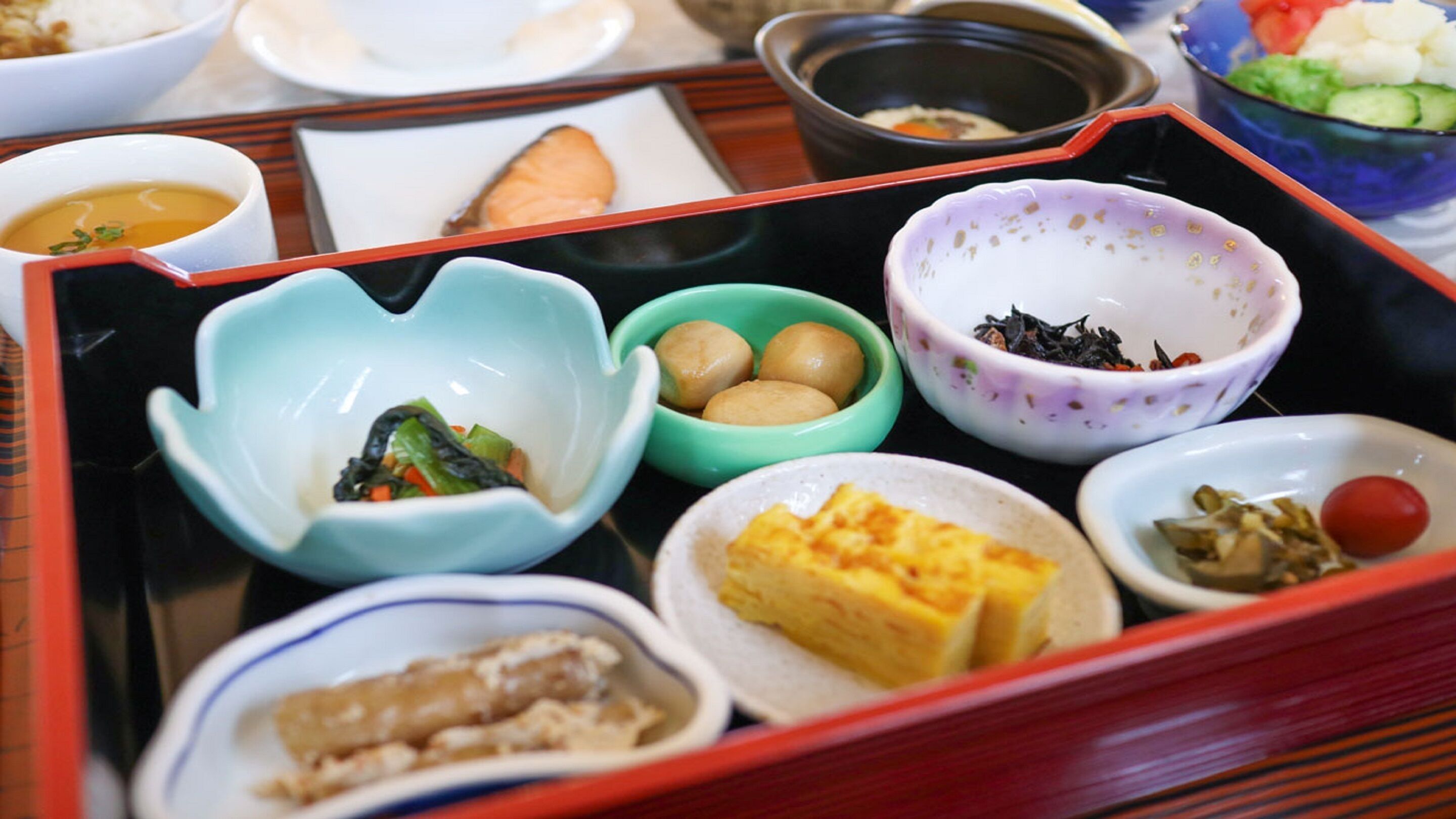 A traditional Japanese bento box with various dishes including sushi, pickled vegetables, and a small bowl of tea.